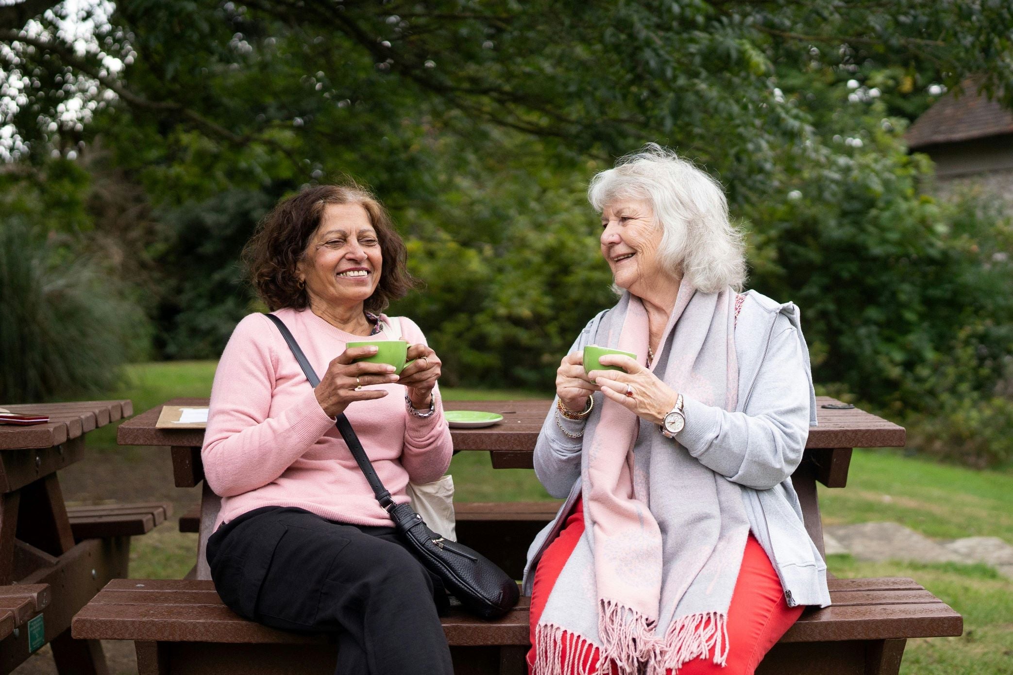 Two elderly woman sitting on a park bench drinking tea